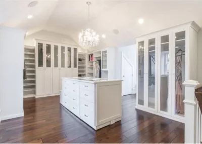 A walk in closet with white cabinets and a chandelier.